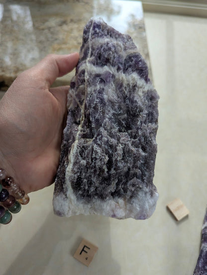Hand displaying a raw Dream Amethyst chunk, showing rough natural textures and vertical banding.