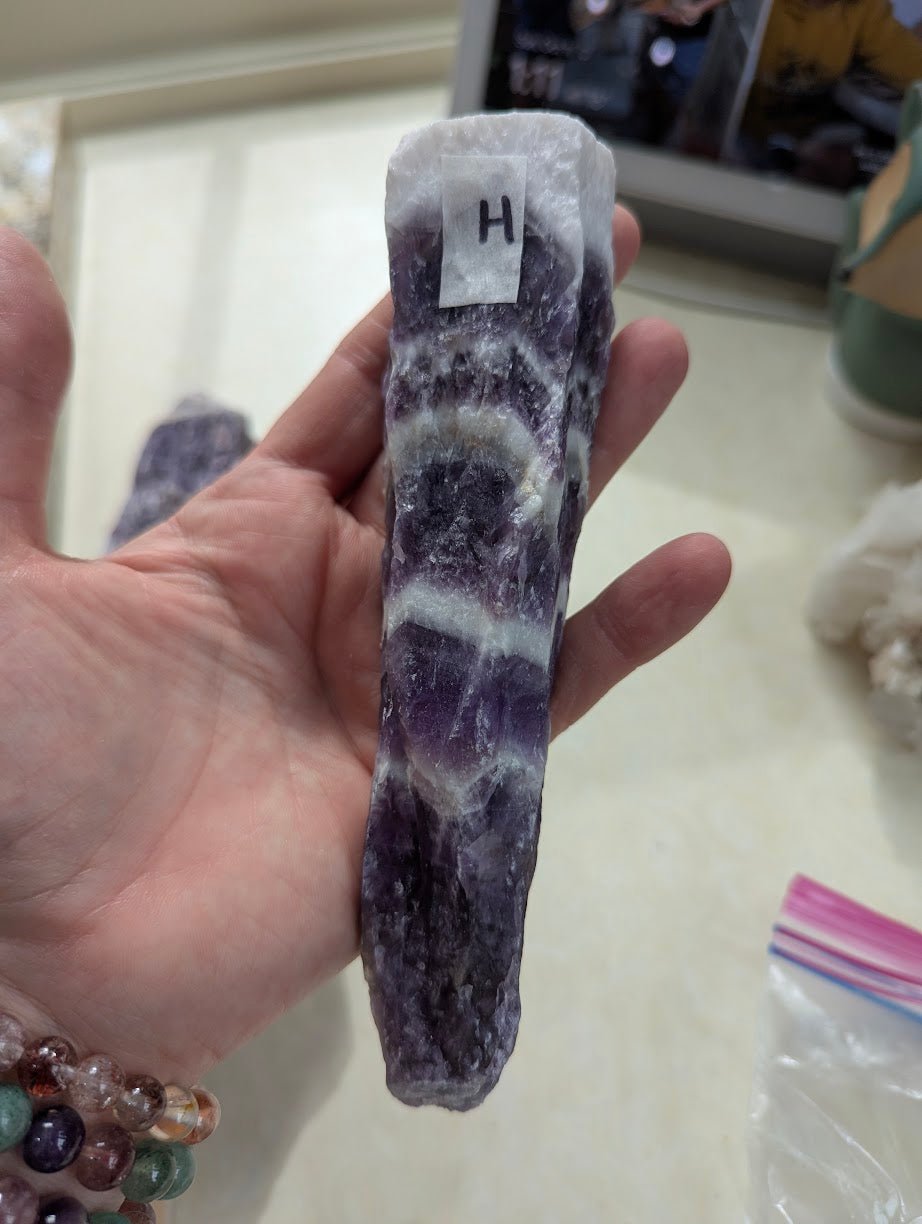Narrow raw Dream Amethyst specimen held in hand, showing sharp, curved chevron banding.