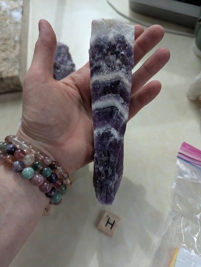 Hand holding a raw Dream Amethyst form, showing a white quartz top and distinct V-shaped purple bands.