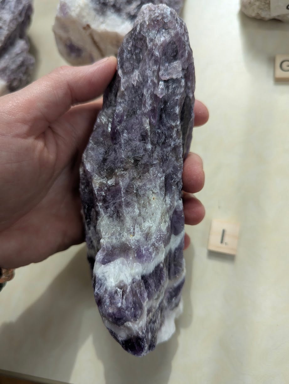 Hand displaying a raw Dream Amethyst chunk, showing its rugged texture and rich purple color saturation.
