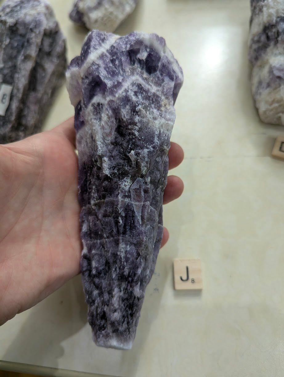 Blocky raw Dream Amethyst specimen held in hand, showing mottled purple hues and natural unpolished edges.
