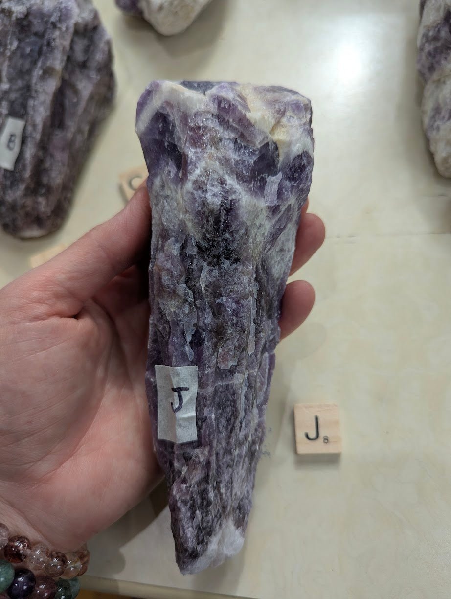 Blocky raw Dream Amethyst specimen held in hand, showing mottled purple hues and natural unpolished edges.