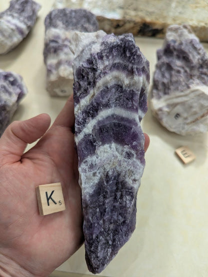 Raw Dream Amethyst specimen held in hand, displaying highly contrasting white quartz and dark purple chevron banding across the front face.