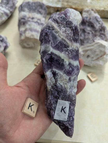 Hand holding a raw Dream Amethyst chunk, showing the rugged side profile and saturated purple colouration.