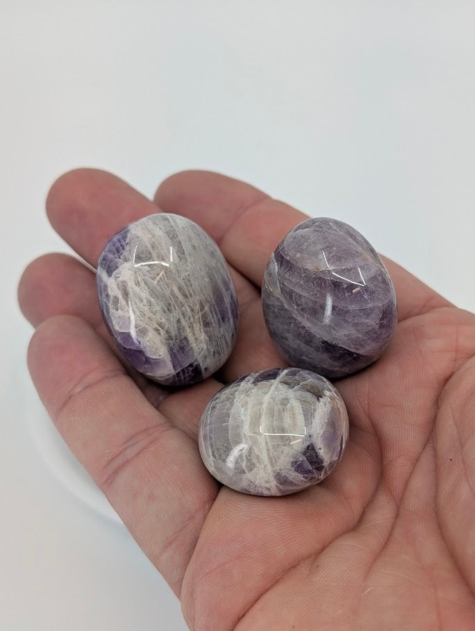 Dream Amethyst tumbled stones in hand for size reference