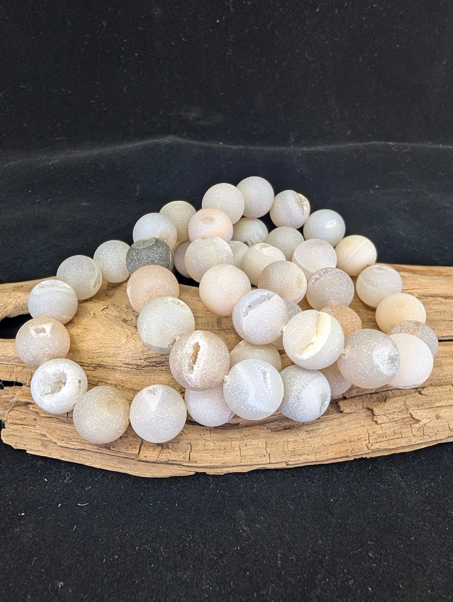 Full view of a 14mm Druzy Agate bracelet on driftwood, featuring matte beads with open crystal vugs.