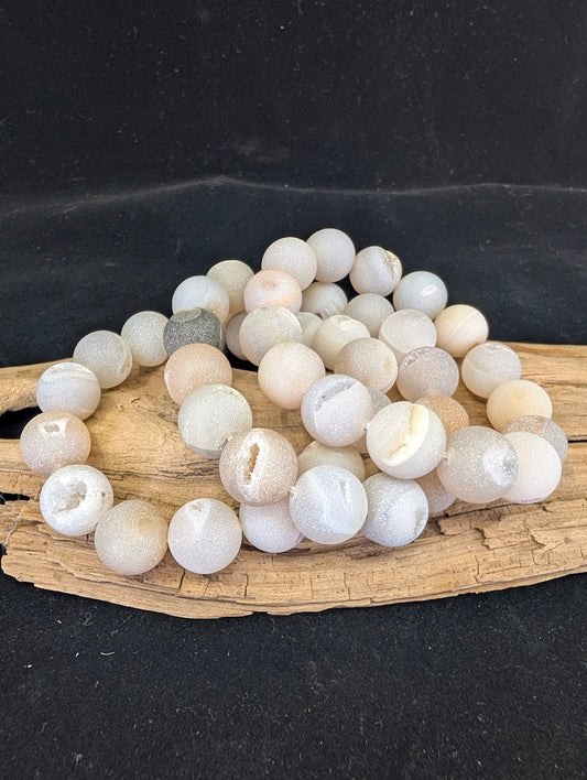 Full view of a 14mm Druzy Agate bracelet on driftwood, featuring matte beads with open crystal vugs.