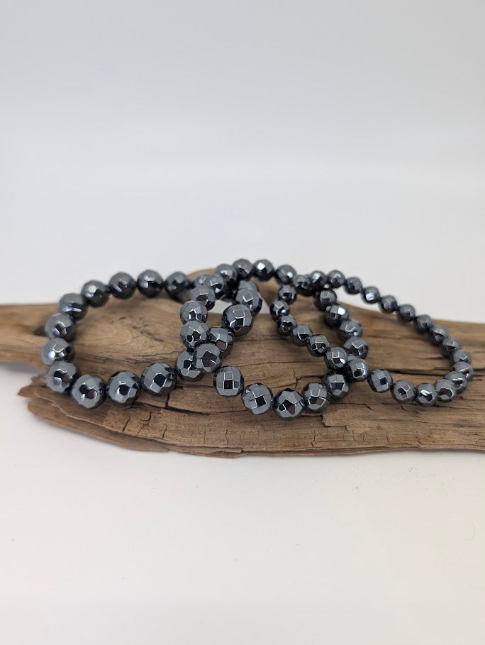 Faceted natural hematite bracelets in 8mm, 10mm, and 12mm displayed on driftwood