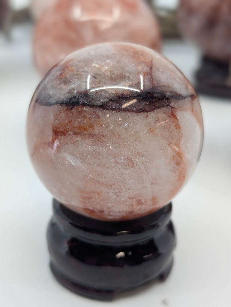 Studio portrait orientation of Brazilian Fire Quartz sphere FQ-10, showcasing the distinct horizontal split between clear and dark red mineral zones.