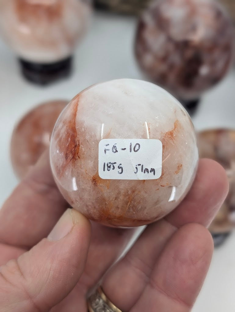 Close-up tracking photo of the base of Brazilian Fire Quartz sphere FQ-10, verified with label marking 185g and 51mm.