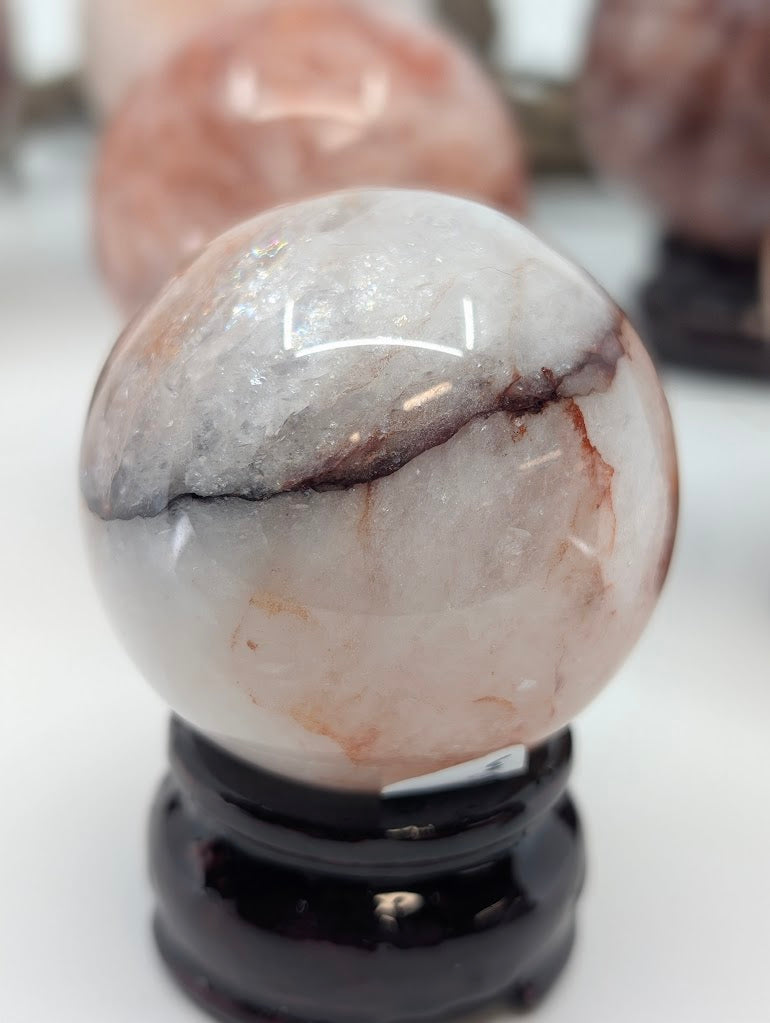 High-angle portrait shot of Brazilian Hematoid Quartz sphere FQ-10, demonstrating natural rainbow flashes reflecting along internal fracture planes.