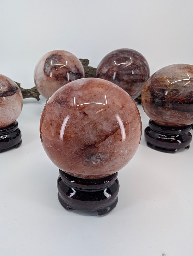 Sidelit view of polished Hematoid Quartz sphere FQ-11 from Brazil, showing fine needle inclusions and cloudy bands inside clear quartz.