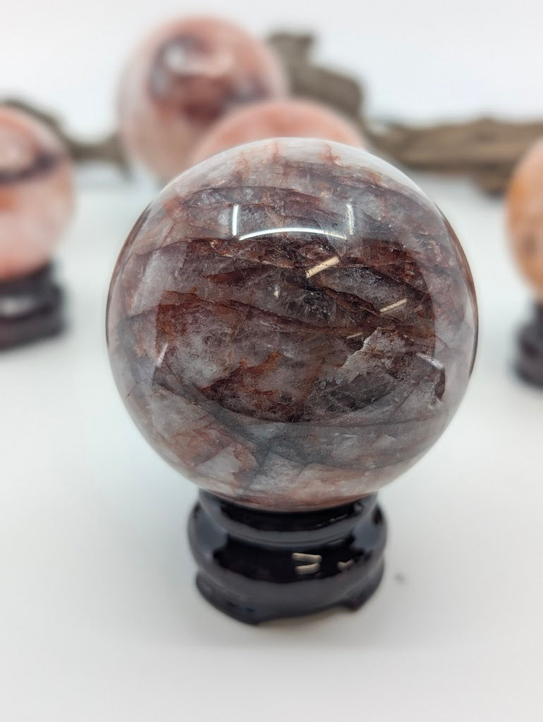 Detailed macro perspective of natural Fire Quartz sphere FQ-13 from Brazil, showcasing intricate webs of red iron veining in quartz.