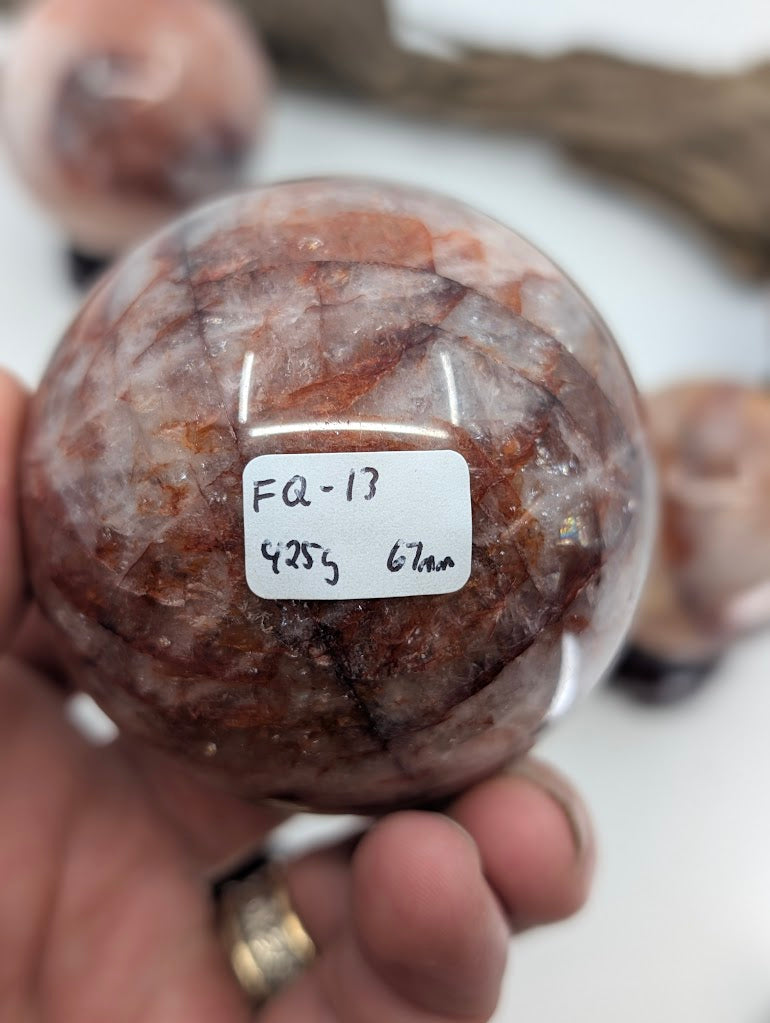 Collector hand scale verification photo of Brazilian Fire Quartz sphere FQ-13, showing the tracking label marked 280 grams and 59mm.
