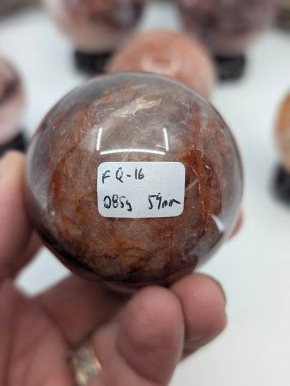 Collector hand scale verification photo of Brazilian Hematoid Quartz sphere FQ-16, showing the tracking label marked 285 grams and 59mm.