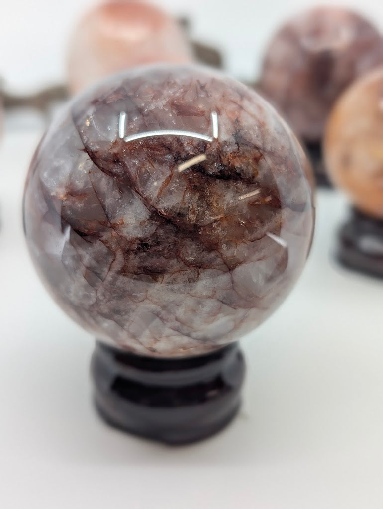 Detailed visual focus on the prominent chocolate-maroon hematite cap and dark red lines crossing polished Fire Quartz sphere FQ-15 from Brazil.
