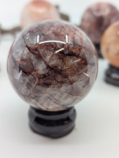 Detailed visual focus on the prominent chocolate-maroon hematite cap and dark red lines crossing polished Fire Quartz sphere FQ-15 from Brazil.