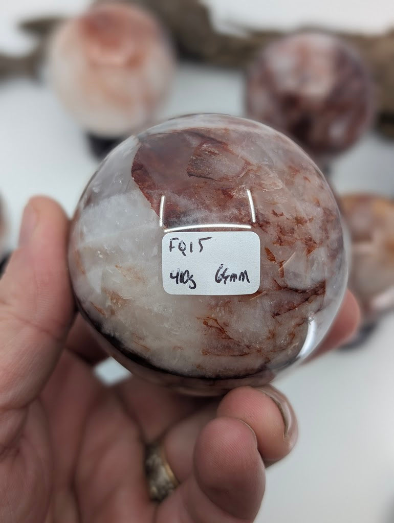 Collector hand scale verification photo of substantial Brazilian Hematoid Quartz sphere FQ-15, showing the tracking label marked 410 grams and 64mm.