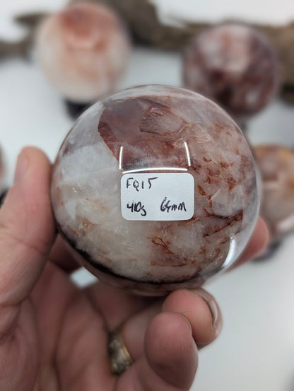 Collector hand scale verification photo of substantial Brazilian Hematoid Quartz sphere FQ-15, showing the tracking label marked 410 grams and 64mm.