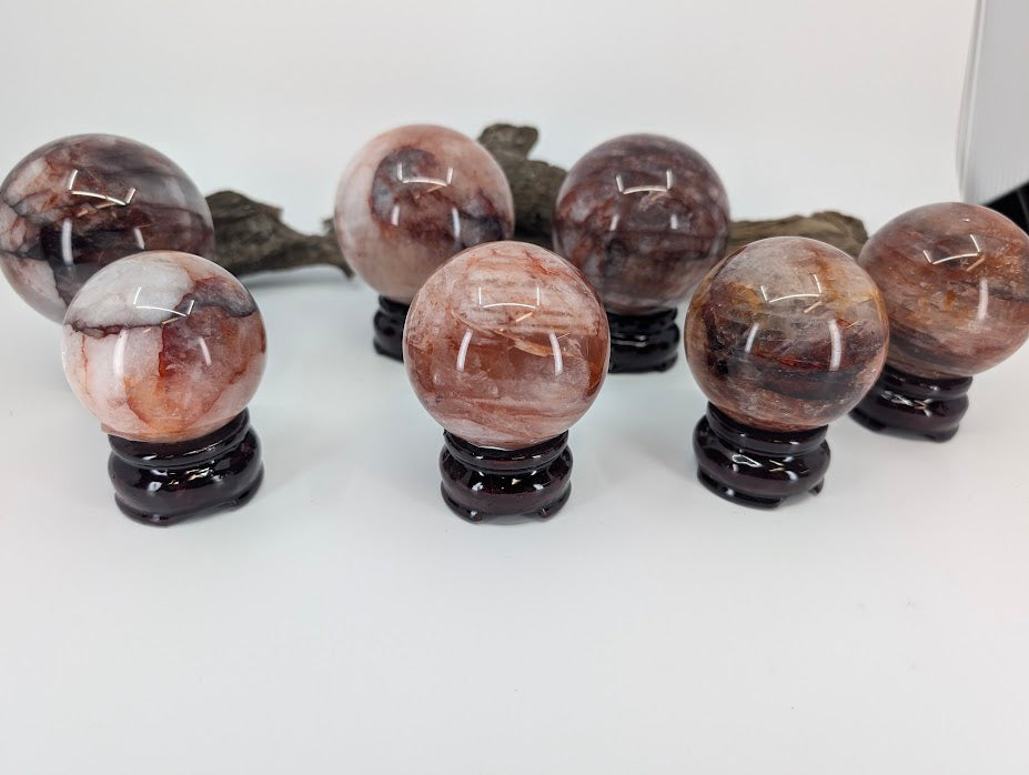 Linear group display of all seven polished Brazilian Fire Quartz spheres on their matching dark wooden stands, organized by size and visual density.