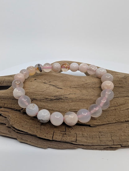 Flower Agate 8mm round bead stretch bracelet on driftwood showing blush-pink tones and white plume “flowers”