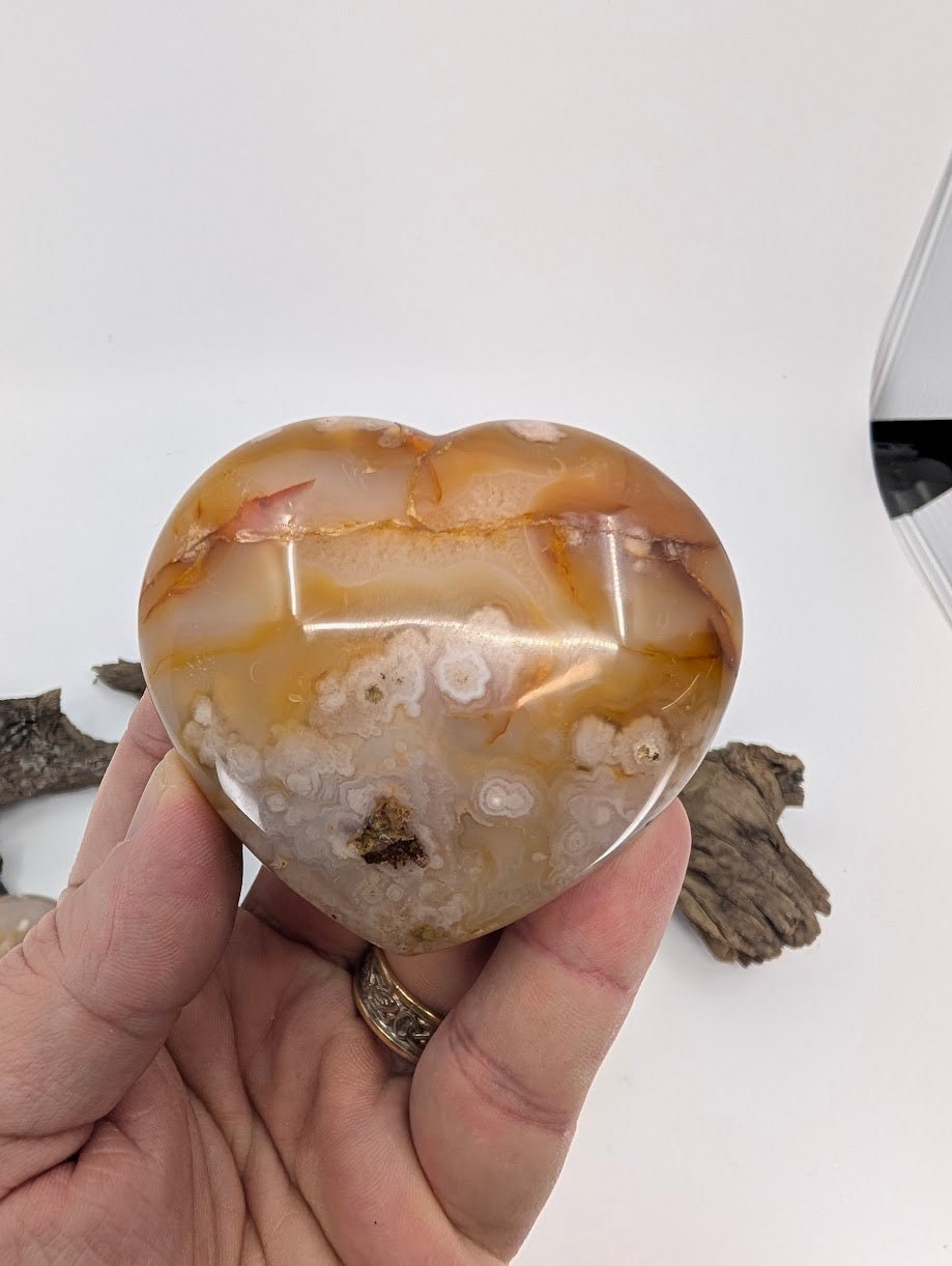 Hand holding Specimen B, a 220g Flower Agate heart with distinct white flowers.