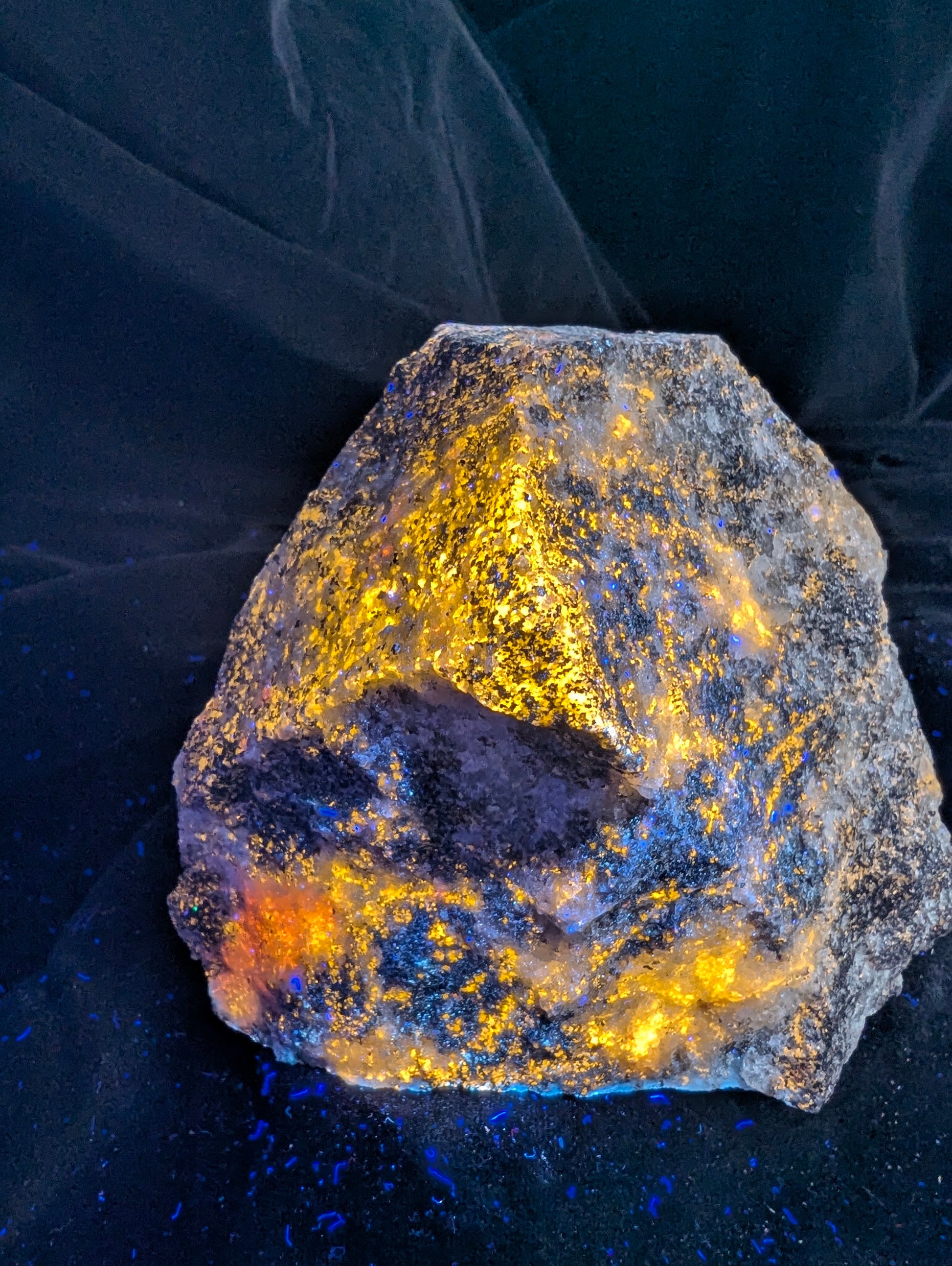 An angled view of the fluorescent Scapolite Trevorite specimen from Bancroft, Ontario, under longwave UV light. It glows bright yellow and orange across its multiple faces, showcasing high concentration and reactivity.