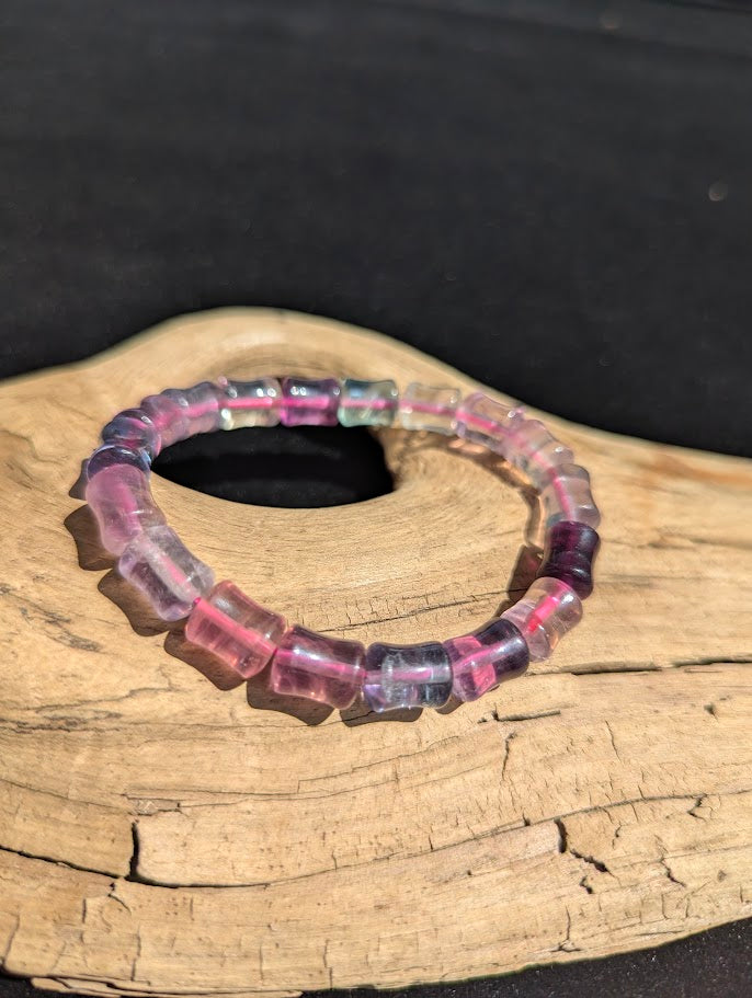 7mm polished Fluorite bamboo bead stretch bracelet resting on a driftwood display, showing translucent purple and clear zones strung on a pink elastic cord.