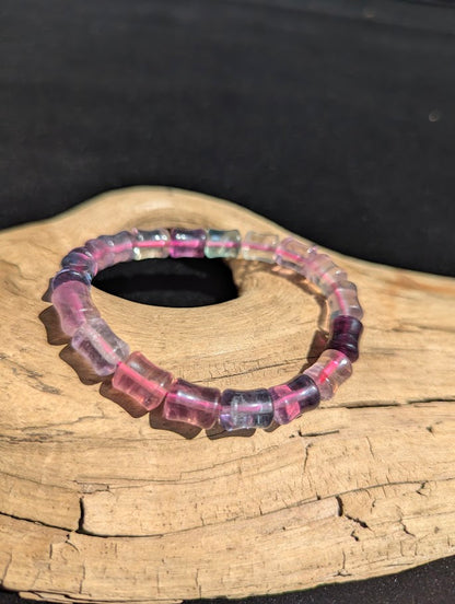 7mm polished Fluorite bamboo bead stretch bracelet resting on a driftwood display, showing translucent purple and clear zones strung on a pink elastic cord.