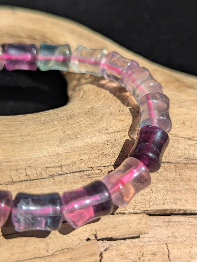 Macro close-up of 7mm polished Fluorite bamboo beads highlighting the unique cylindrical cut and natural colour zoning over a bright pink elastic cord.