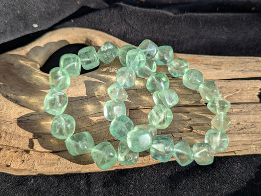 An 11.5mm Green Fluorite cube bead stretch bracelet resting on a neutral presentation surface, demonstrating exceptional lapidary polish and deep sea-green mineral saturation.