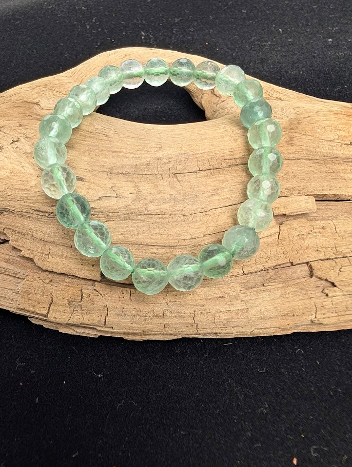 8mm faceted green Fluorite beaded stretch bracelet resting on a driftwood display, showing translucent pale green tones.
