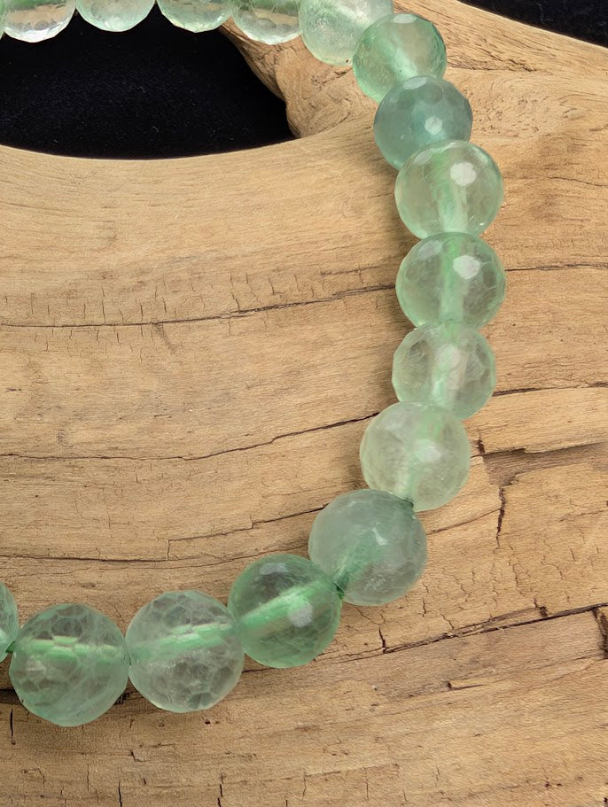 Macro close-up of 8mm faceted green Fluorite beads highlighting geometric surface cuts and a green stretch cord.