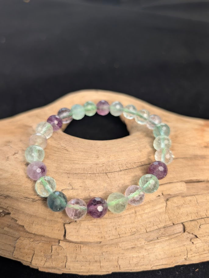 8mm faceted purple and green Fluorite beaded stretch bracelet resting on a driftwood display, showing translucent colour zoning.