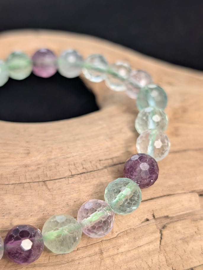 Macro close-up of 8mm faceted purple and green Fluorite beads highlighting internal cleavage planes and geometric surface cuts.