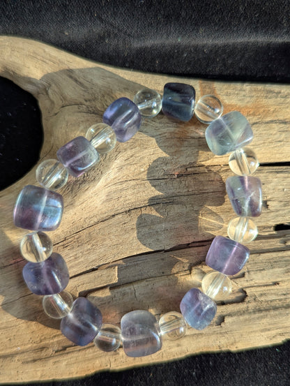 A 9 mm blue fluorite cube and 8 mm clear quartz round bead stretch bracelet positioned on a neutral presentation surface, demonstrating precise geometric lapidary cuts and high structural contrast.