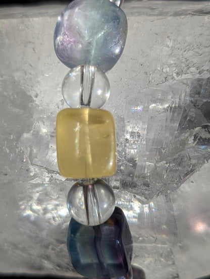 Mixed-colour fluorite and clear quartz stretch bracelet worn on the wrist, highlighting the striking visual contrast between the isometric and rounded bead shapes under balanced lighting.