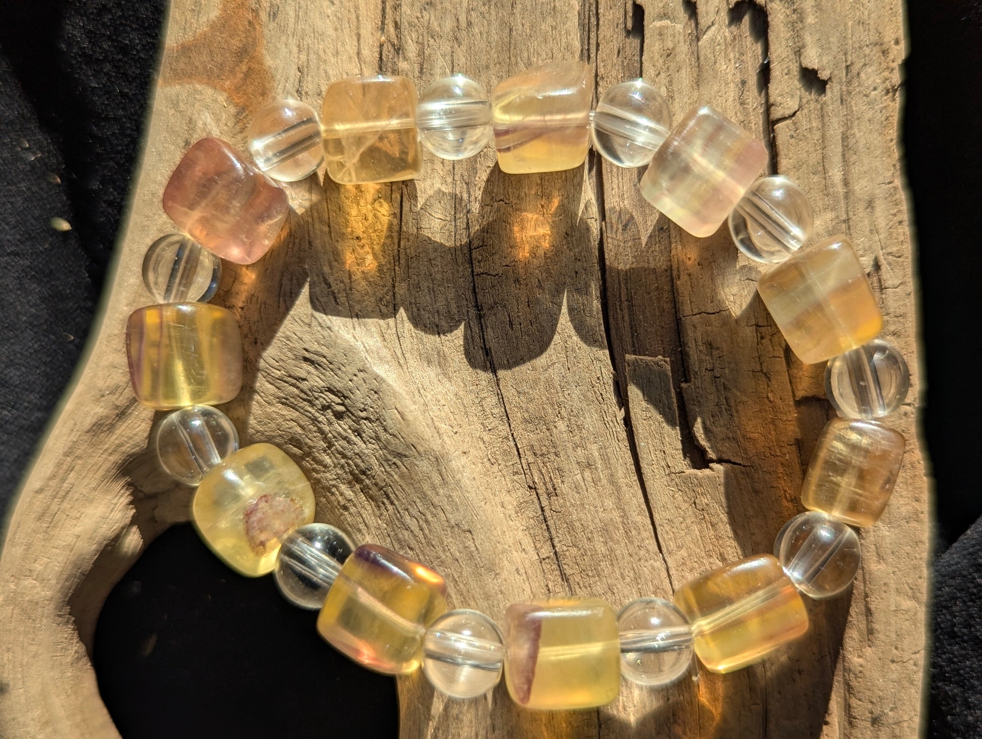 A 9 mm yellow fluorite cube and 8 mm clear quartz round bead stretch bracelet positioned on a neutral presentation surface, showcasing warm golden translucency against brilliant clear spheres.