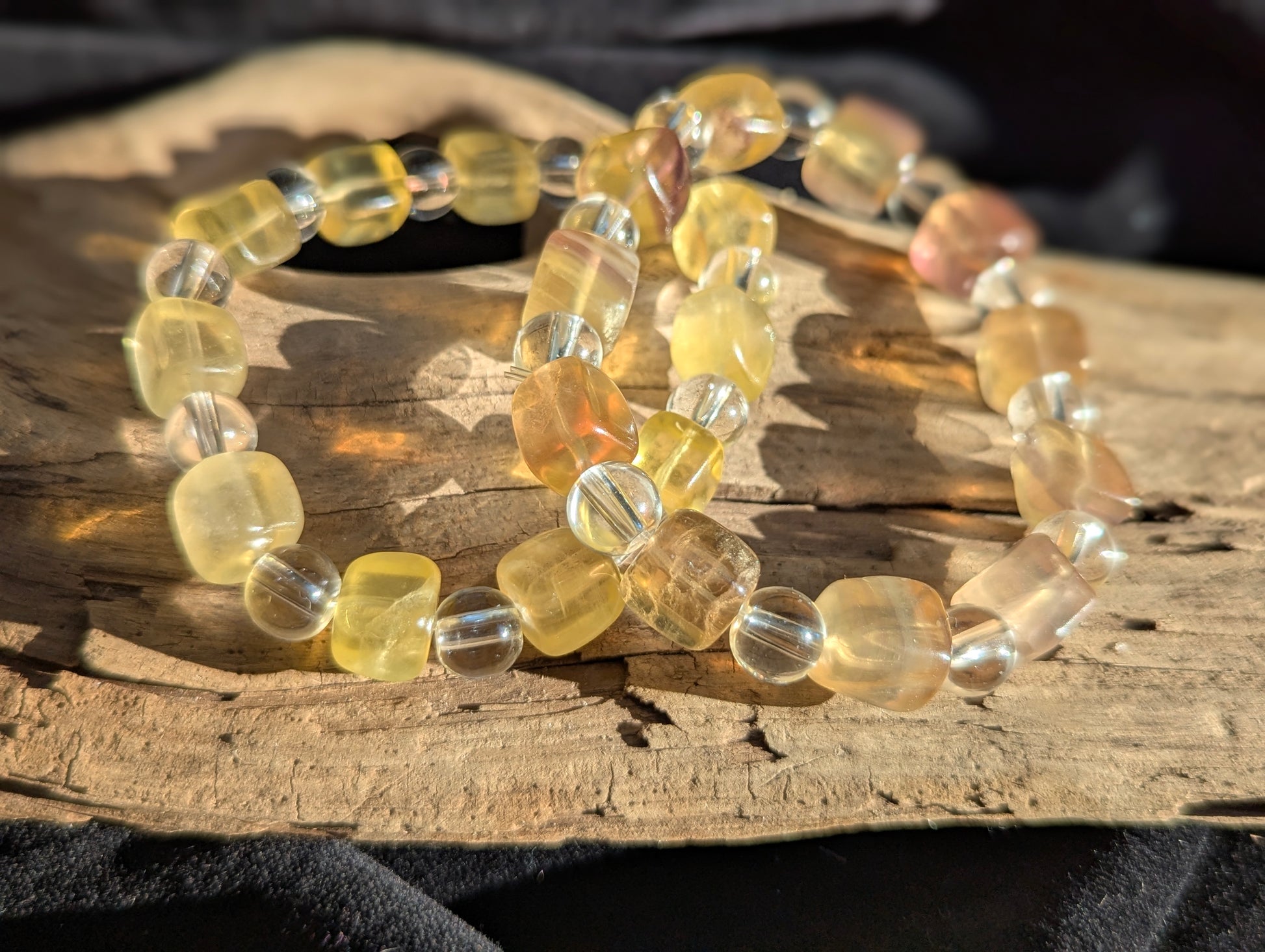 A 9 mm yellow fluorite cube and 8 mm clear quartz round bead stretch bracelet positioned on a neutral presentation surface, showcasing warm golden translucency against brilliant clear spheres.
