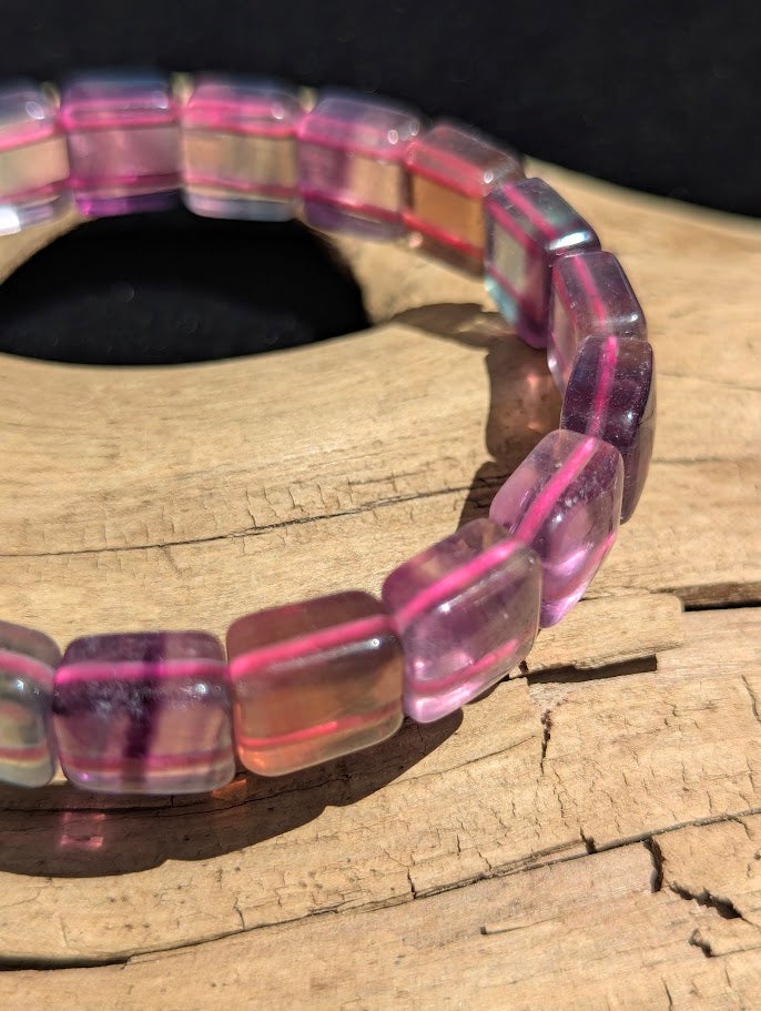 Macro close-up of polished Fluorite square segment beads highlighting the geometric cut, high translucency, and natural colour zoning over a bright pink elastic cord.