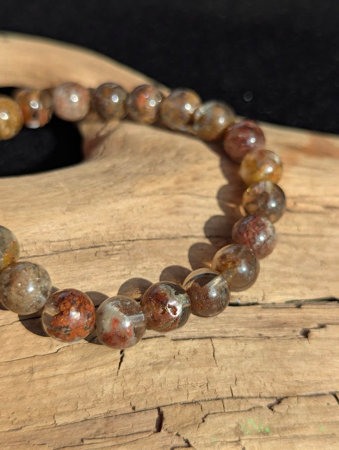 Macro photograph of 8mm Garden Quartz beads highlighting the natural red, yellow, and green scenic inclusions suspended within clear quartz.