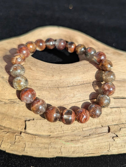 Intuitively selected 9mm AA Grade Four Season Garden Quartz beaded stretch bracelet resting on driftwood, showcasing excellent optical clarity.