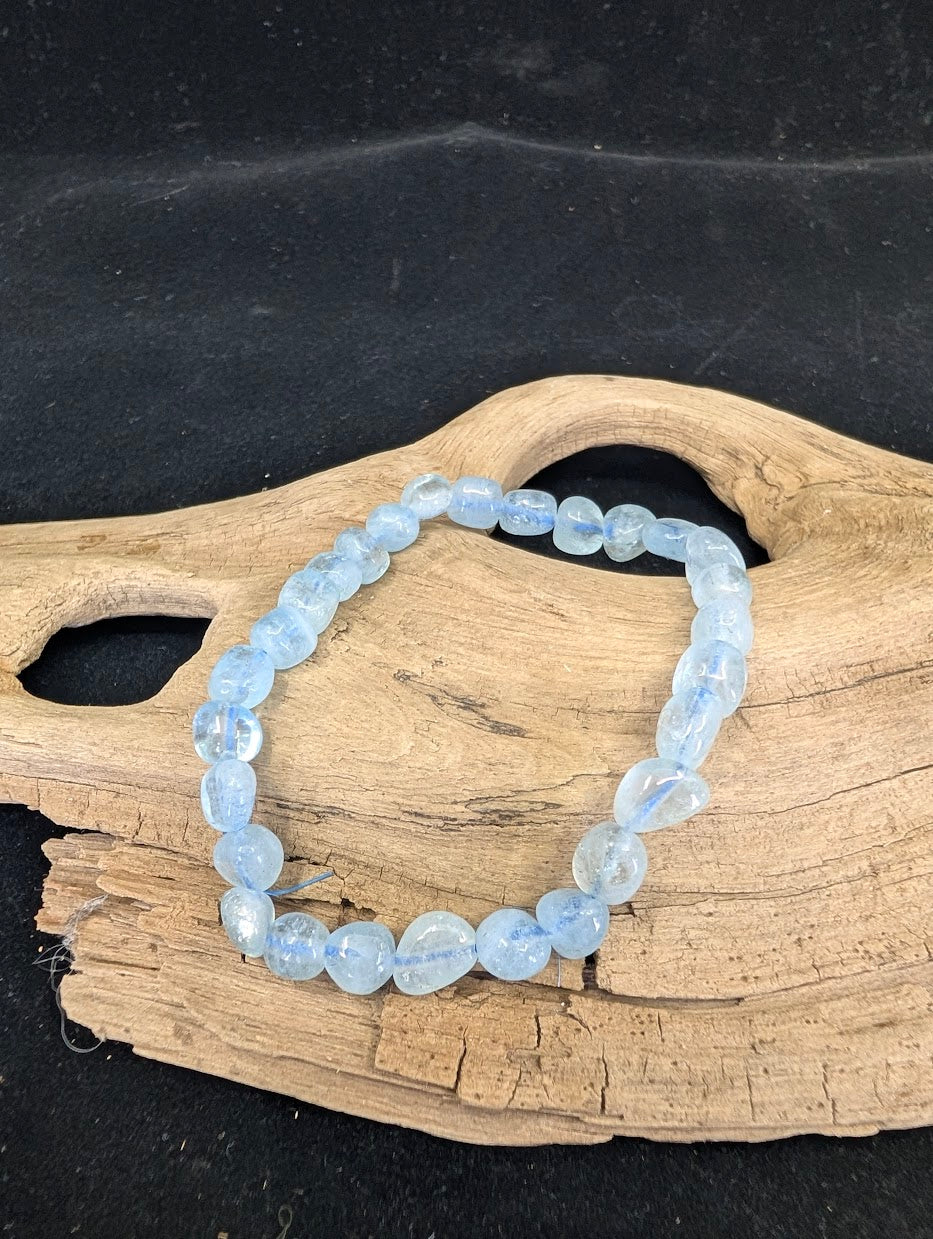 Close-up of a freeform Aquamarine nugget bracelet on a natural wood base, showing icy blue tones.