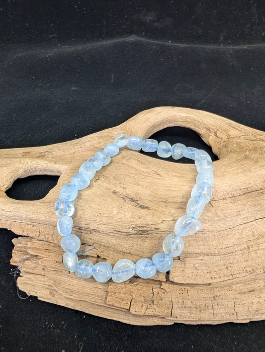 Close-up of a freeform Aquamarine nugget bracelet on a natural wood base, showing icy blue tones.