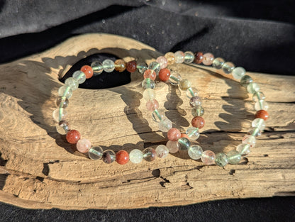 An all-natural 6mm Garden Quartz beaded stretch bracelet with rich green chlorite inclusions, displayed on a neutral surface to show bead uniformity.
