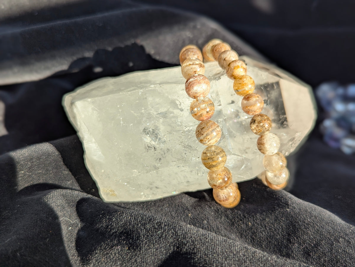 Garden Quartz bracelet draped over a raw clear mineral specimen, contrasting the smooth spherical beads with the rough natural matrix.