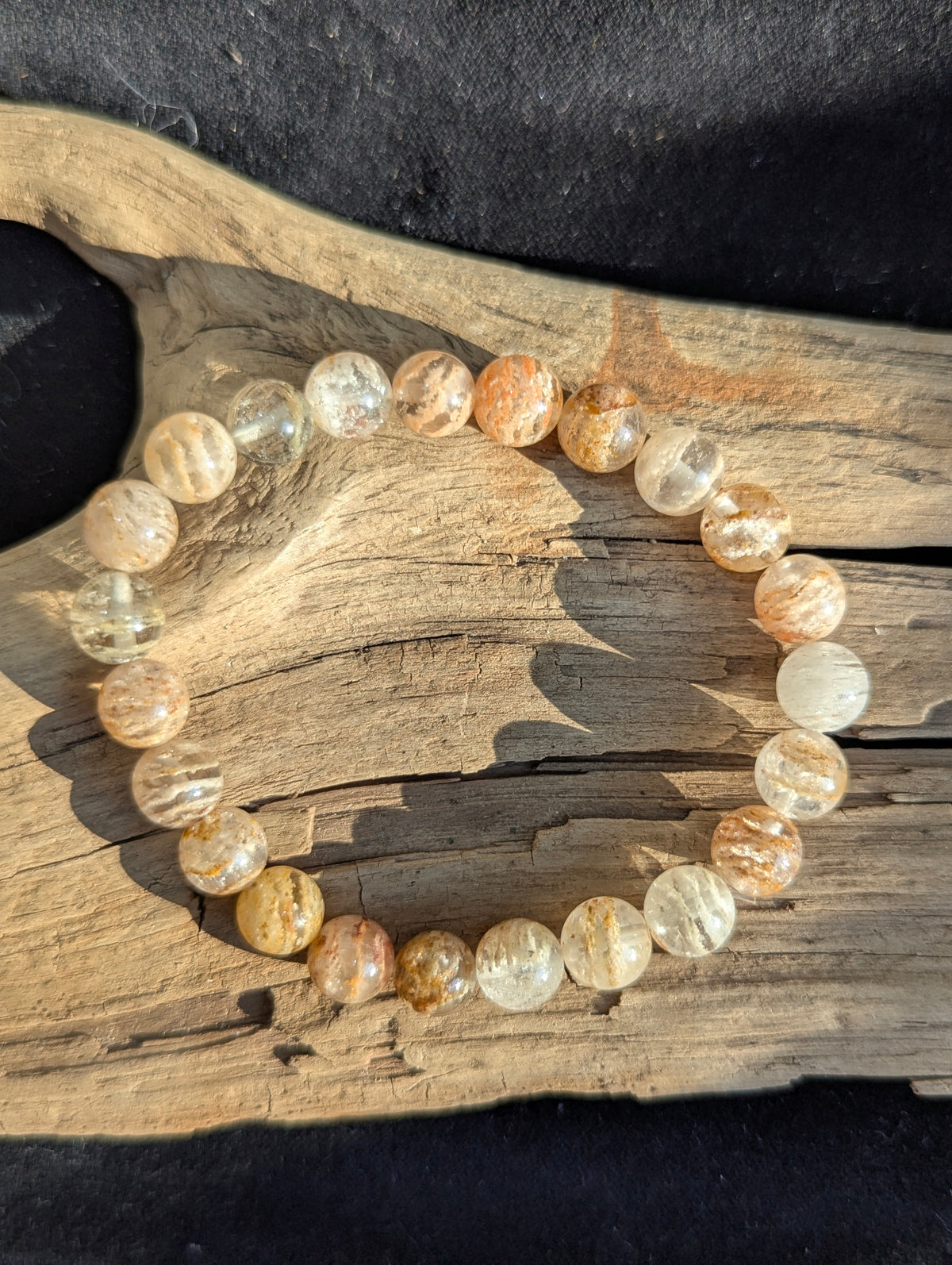 Angled view of a polished Garden Quartz bracelet on driftwood, highlighting the clear quartz matrix and terraced rust-colored mineral layers.