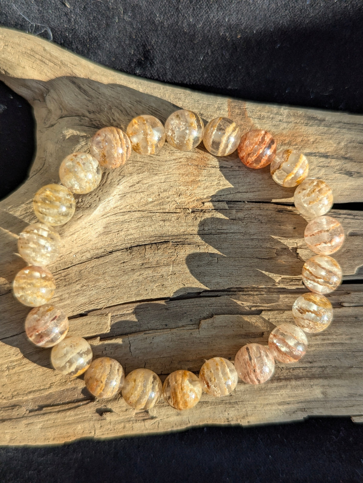 Overhead view of a Garden Quartz bracelet on textured driftwood, showing warm earthy phantom inclusions.