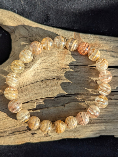 Overhead view of a Garden Quartz bracelet on textured driftwood, showing warm earthy phantom inclusions.