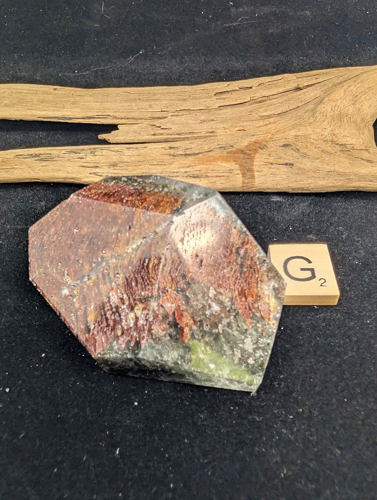 Exact piece Garden Quartz faceted freeform, Variant G2, dominated by a wide, textured layer of ribbed, rust-red iron oxide inclusions.